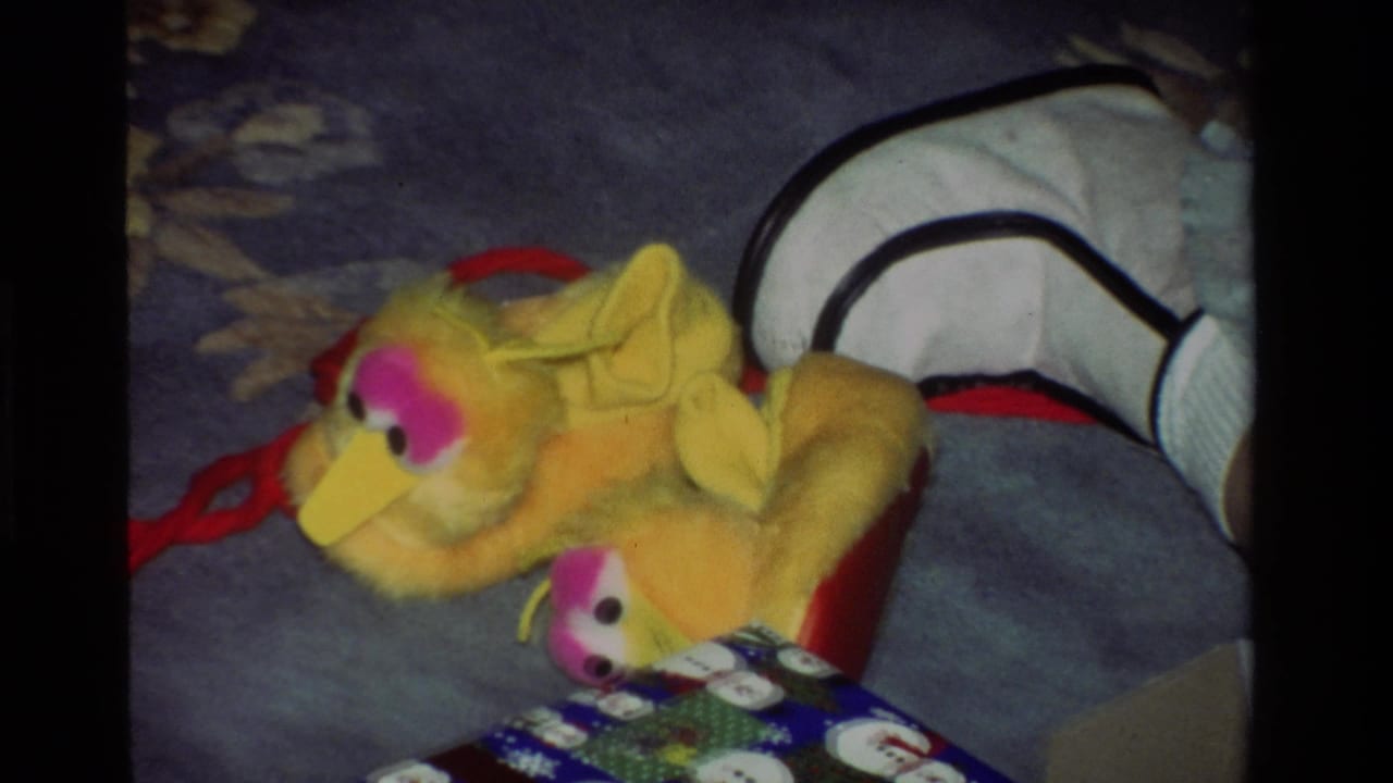 The yellow plush bird toy remains on the blue carpet, with holiday wrapping and a wrapped box visible in the foreground.