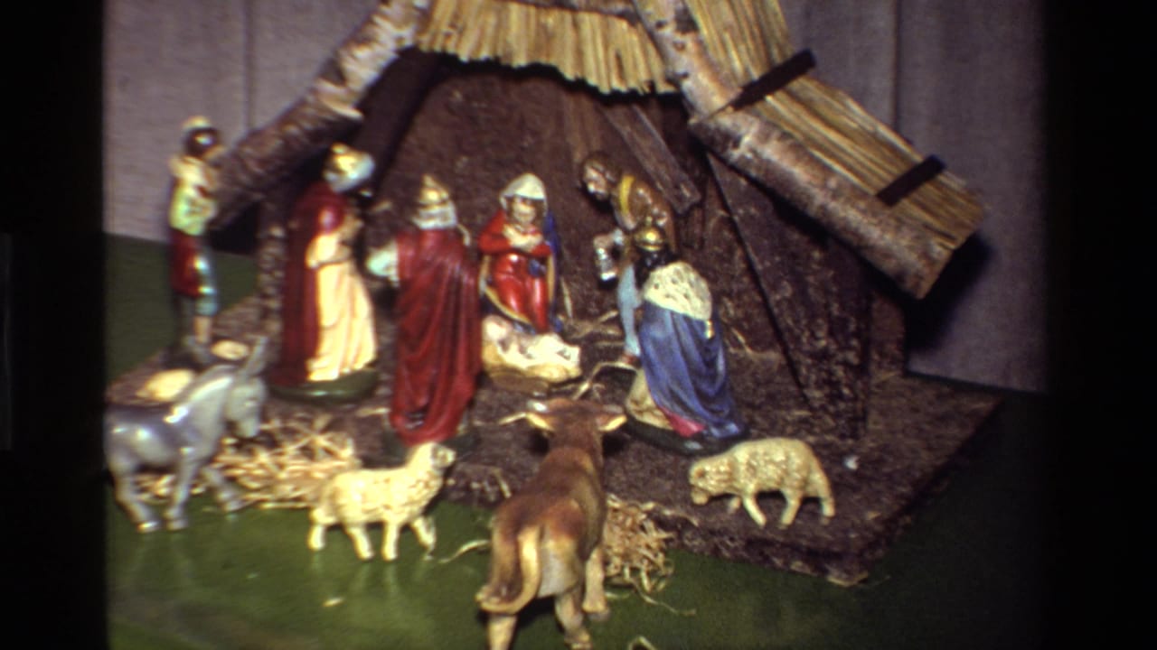 Small Christmas nativity scene with stable, robed figures, straw, sheep, donkey, and cow.