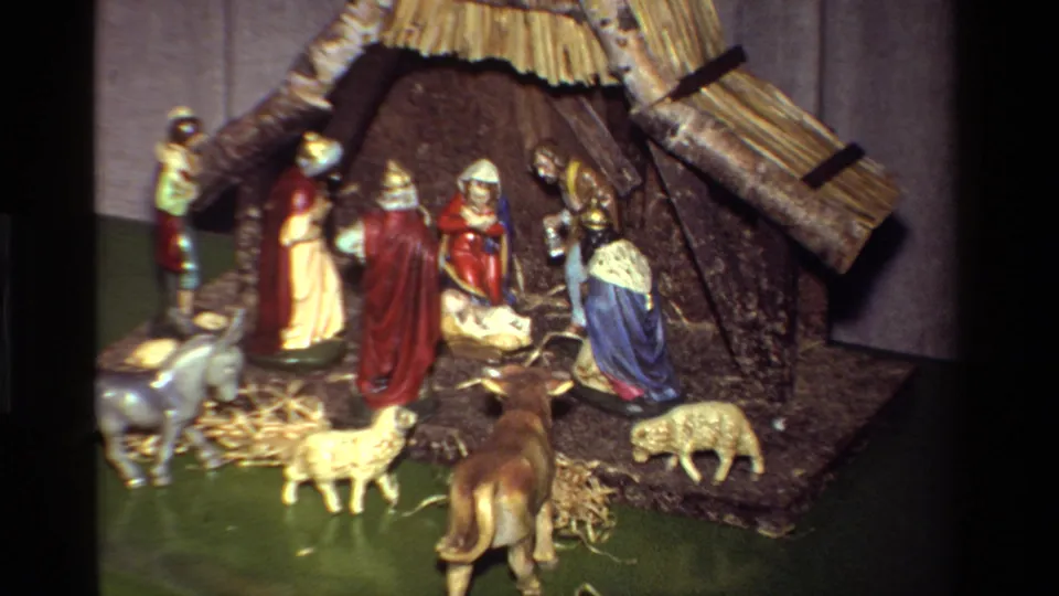 1981 8mm home-movie frame showing a tabletop Christmas nativity display with a rustic stable, Mary and Joseph figures, baby Jesus, animals, and straw.