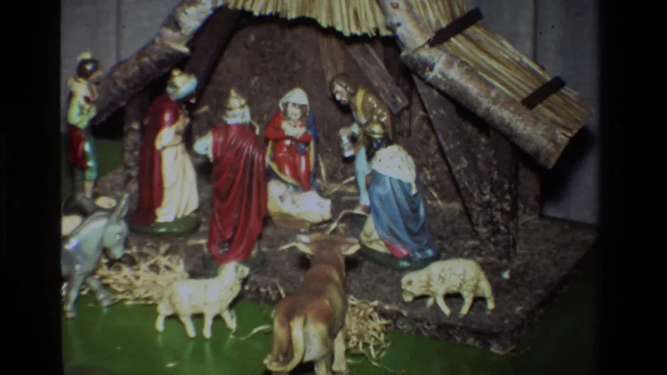 1981 8mm home-movie frame showing a painted Christmas nativity set with central manger, robed figures, sheep, cow, donkey, straw, and rustic stable details.