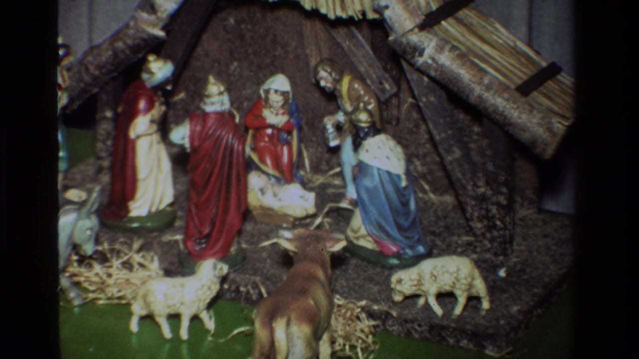 Wide view of a tabletop nativity scene with robed figures, animals, straw, and a rustic stable.