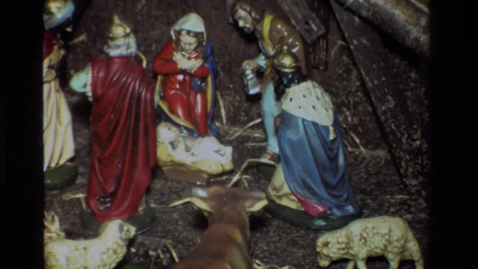 Close 1981 8mm frame of the nativity center in California, showing Mary and Joseph near baby Jesus with straw, a sheep, and a foreground animal figure.
