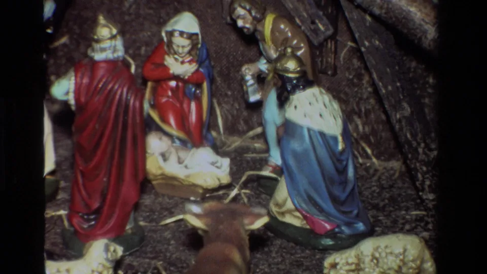 Close 8mm view of a Christmas nativity scene with colorful robed figures, baby Jesus, straw, and small animals.