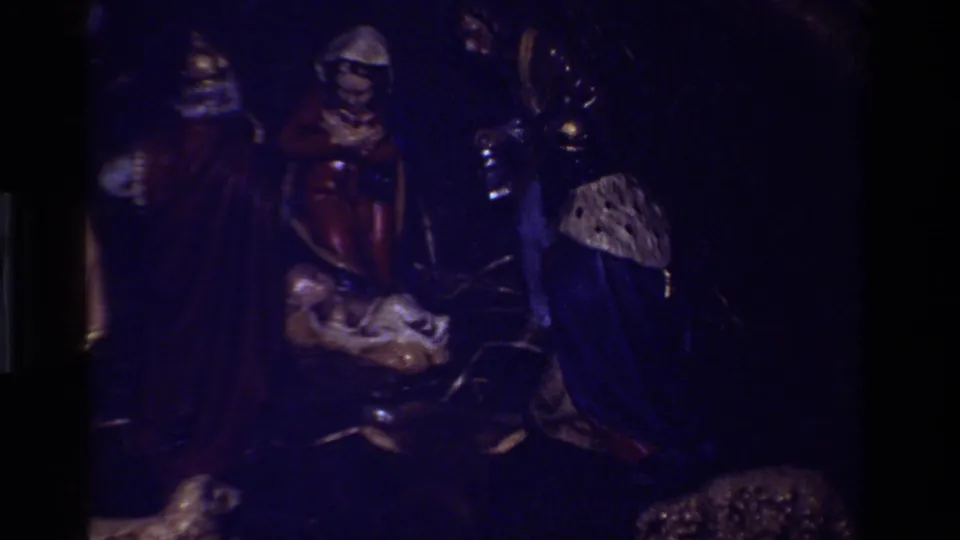 Underexposed 8mm frame where the nativity figures and manger remain faintly visible against a dark blue-black cast.