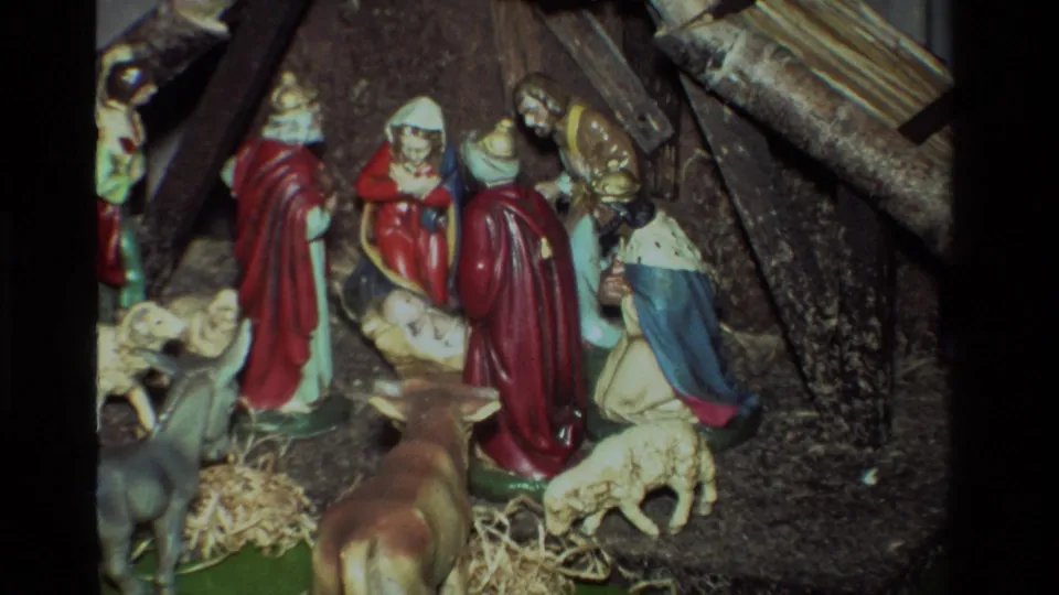 Closer 1981 California 8mm frame of the ceramic nativity figures gathered around baby Jesus, with animals and straw in front.