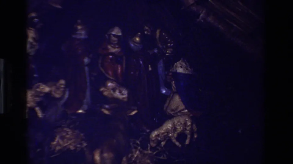 Underexposed blue-tinted 8mm frame from the nativity scene, with robed figures, baby Jesus, and animal figures faintly visible.