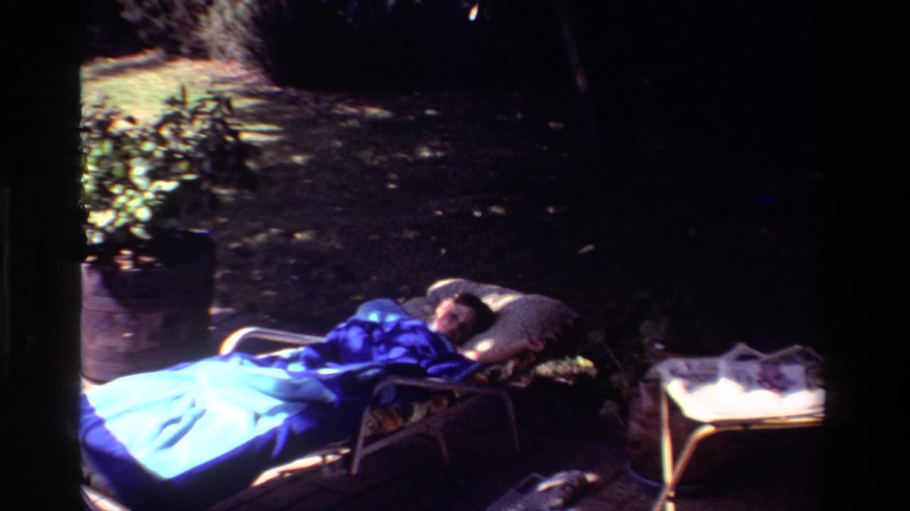 Person lying on an outdoor chaise lounge beside a small table in partial shade.