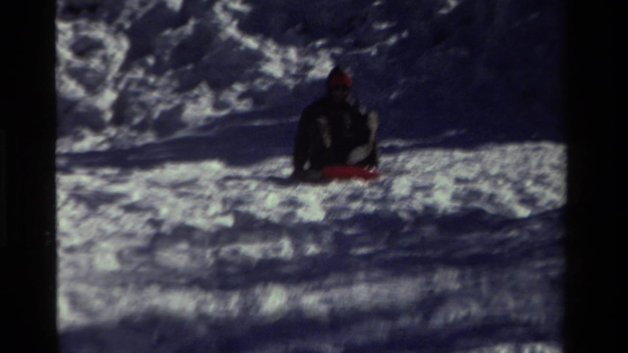 In this 1981 California 8mm frame, a bundled child appears seated on a red sled amid deep snow.