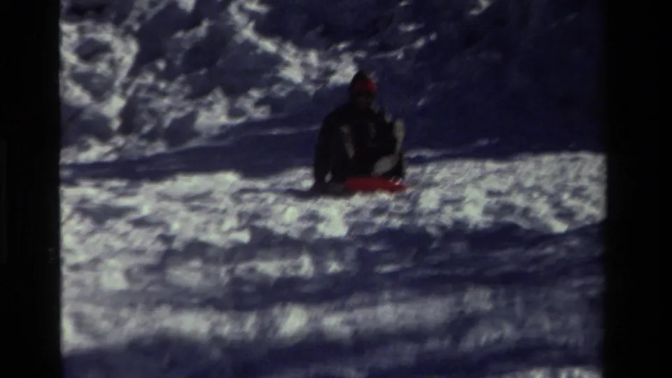 In this 1981 California 8mm frame, a bundled child appears seated on a red sled amid deep snow.