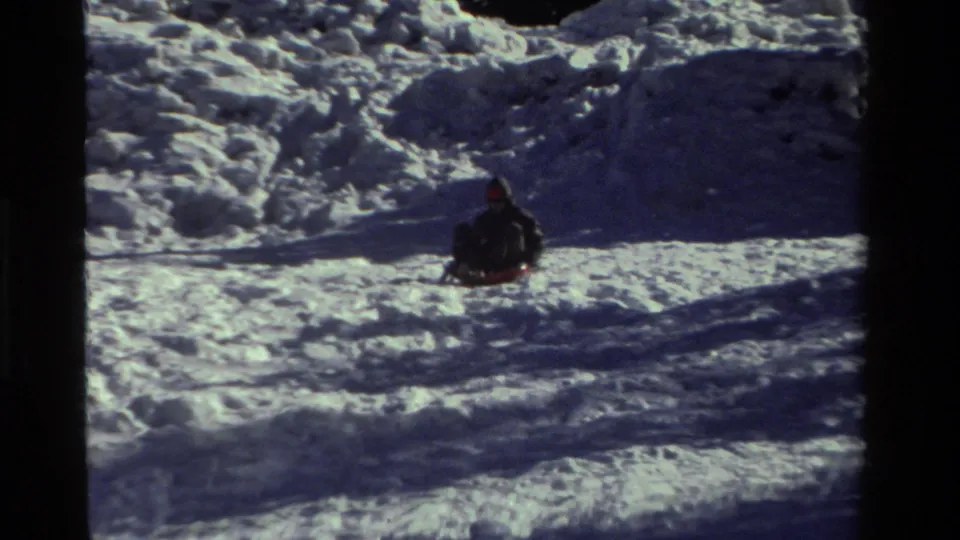 A distant child on a red sled moves downhill through textured snow in this 1981 California home-movie frame.