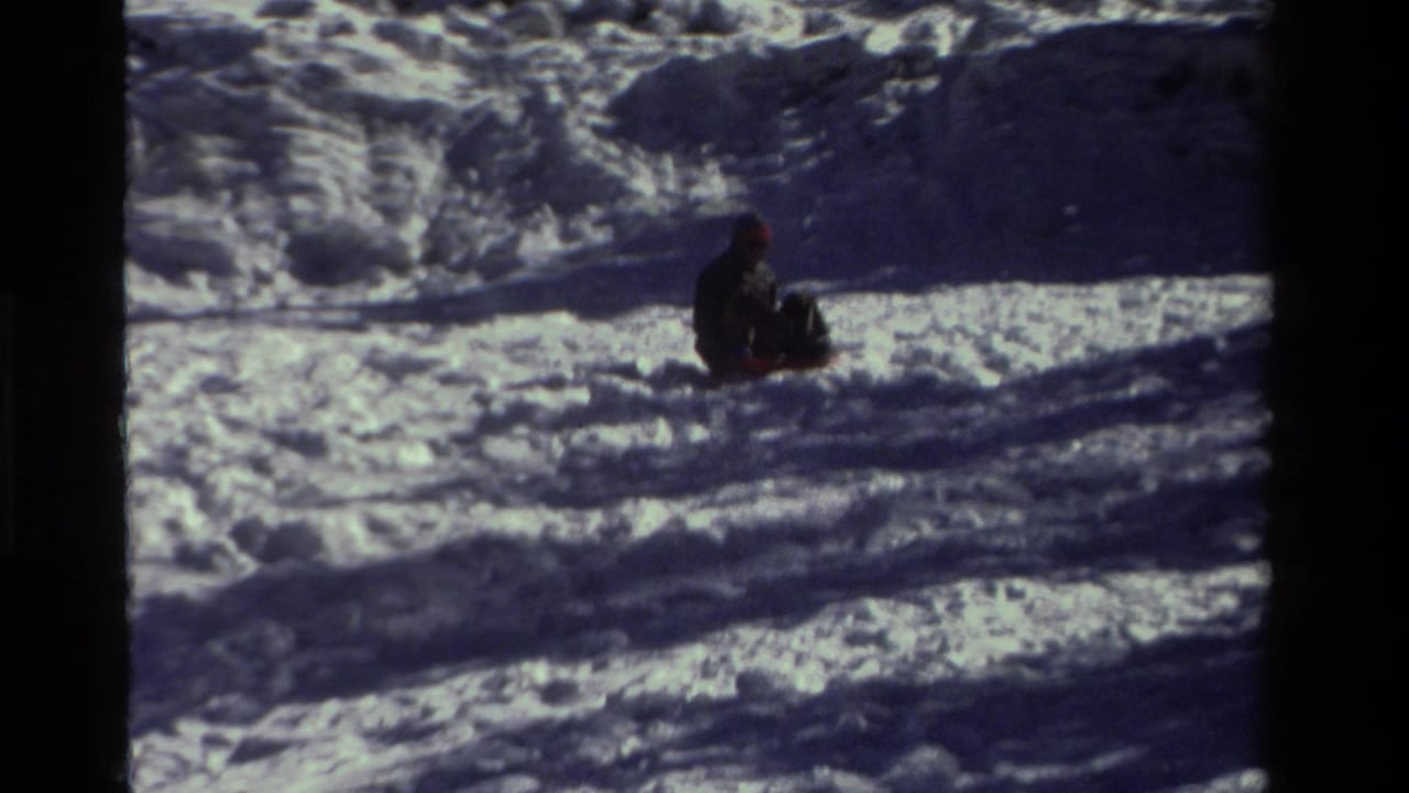 Distant sledder in dark clothing moves across a snowy hillside with deep shadows.