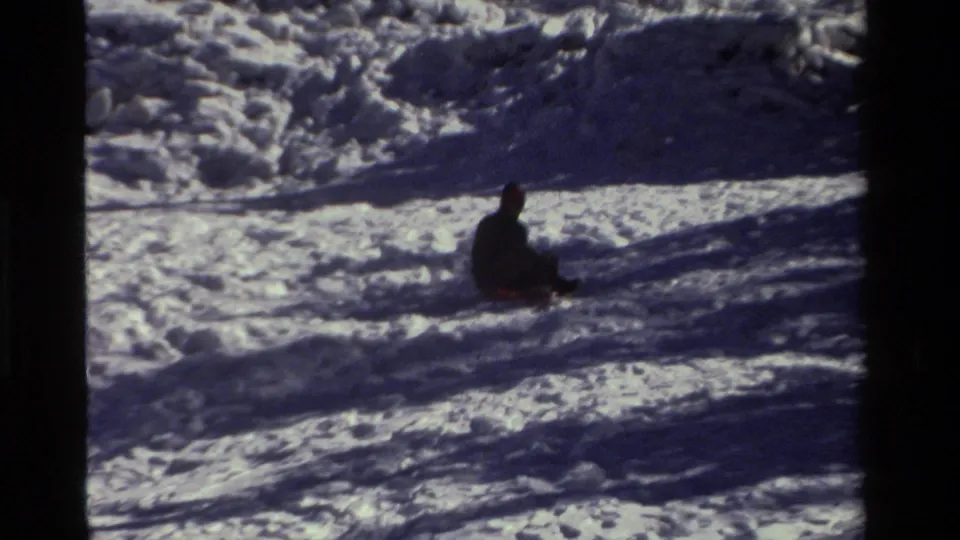 In this 1981 California 8mm frame, a dark-clad sledder sits partway down a bright snowy hill.