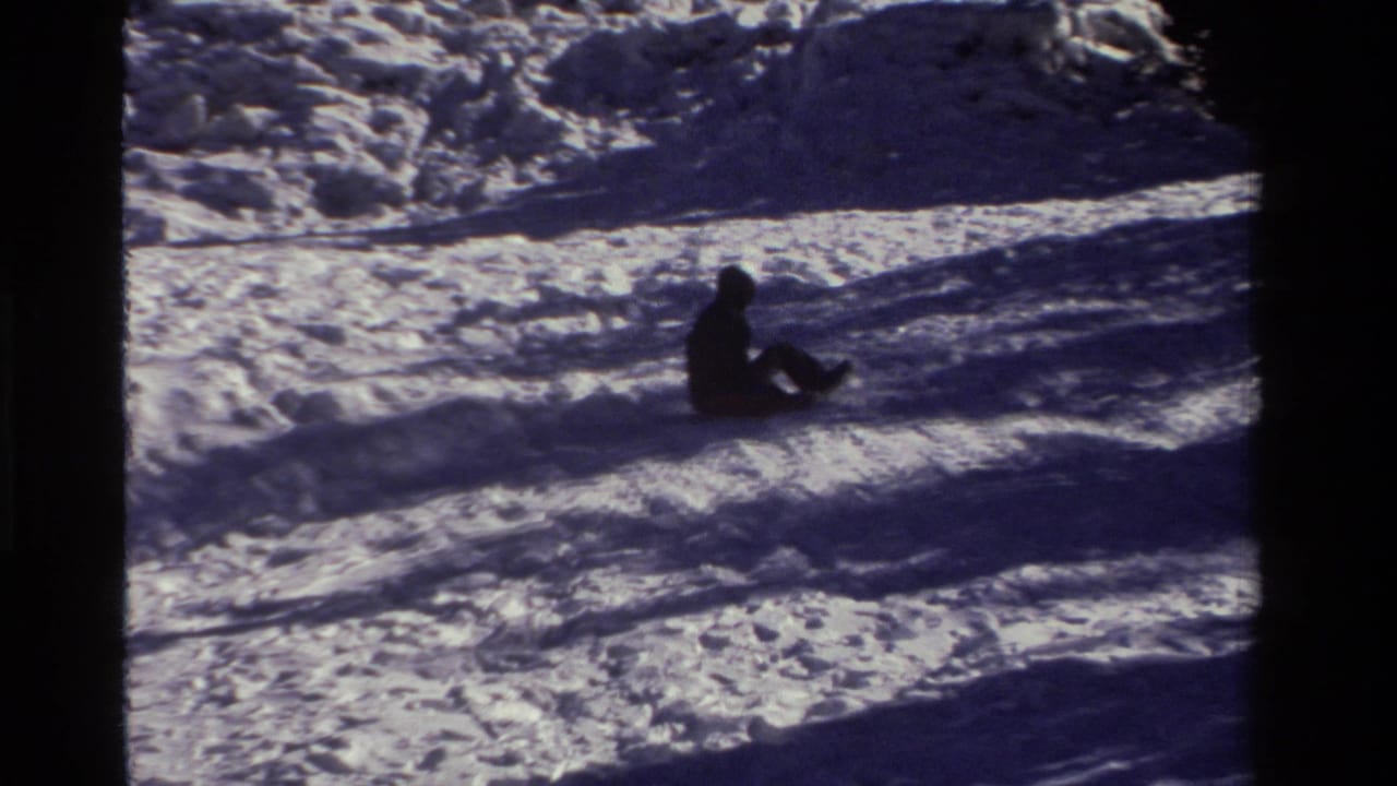 A distant sledder in winter clothing moves across the snow-covered slope in this California home-movie frame.
