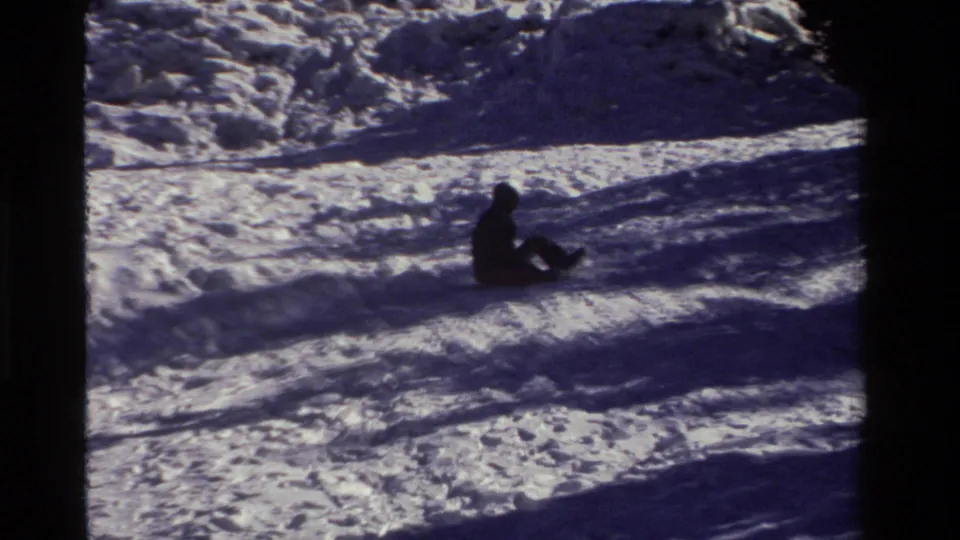 A distant sledder in winter clothing moves across the snow-covered slope in this California home-movie frame.