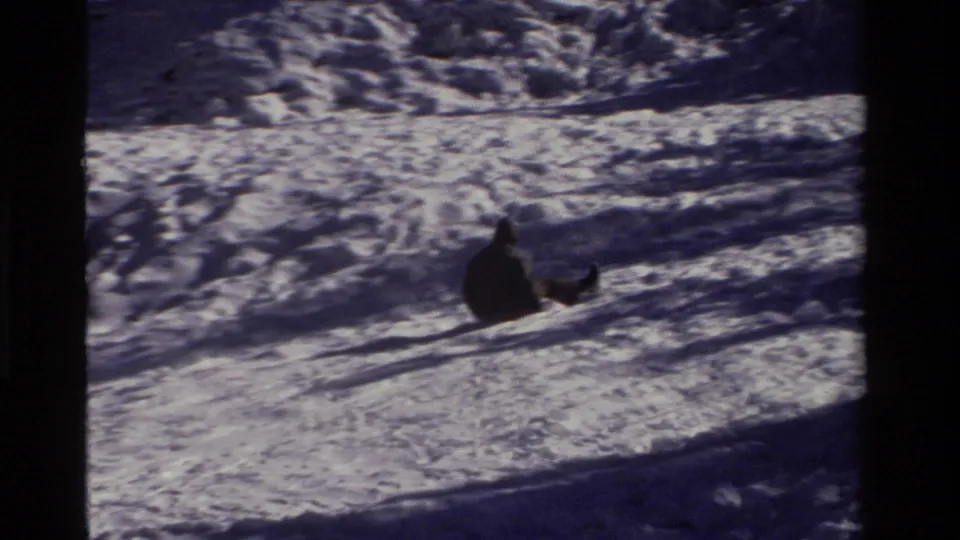 A distant sledder continues down the California snow hill, framed by grainy 8mm borders and strong winter shadows.