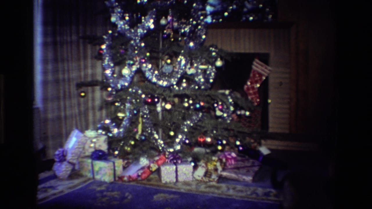 1984 California 8mm frame showing a tinsel-covered Christmas tree with ornaments, wrapped gifts, and a stocking in a dark living room.