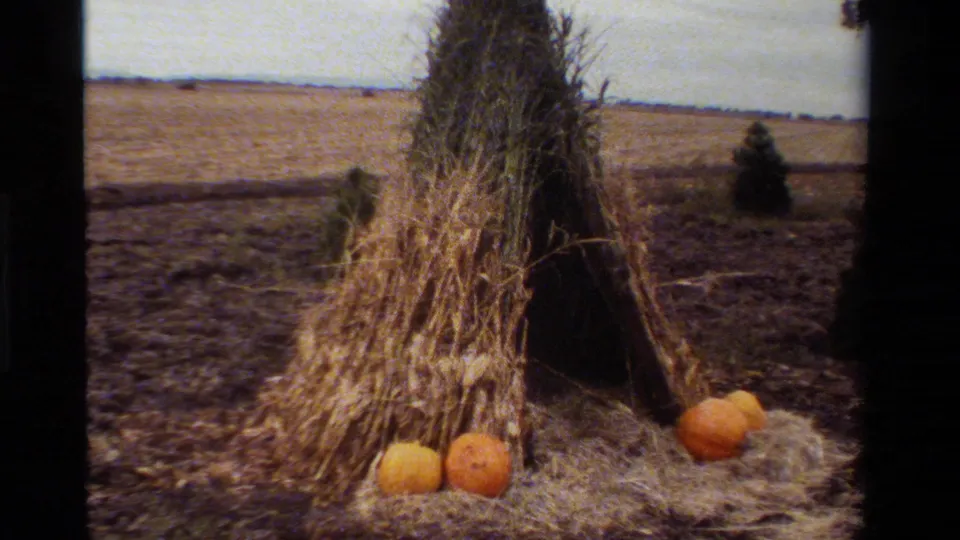 1984 California 8mm frame showing a hay teepee decoration with pumpkins near a rural dirt road and open field.