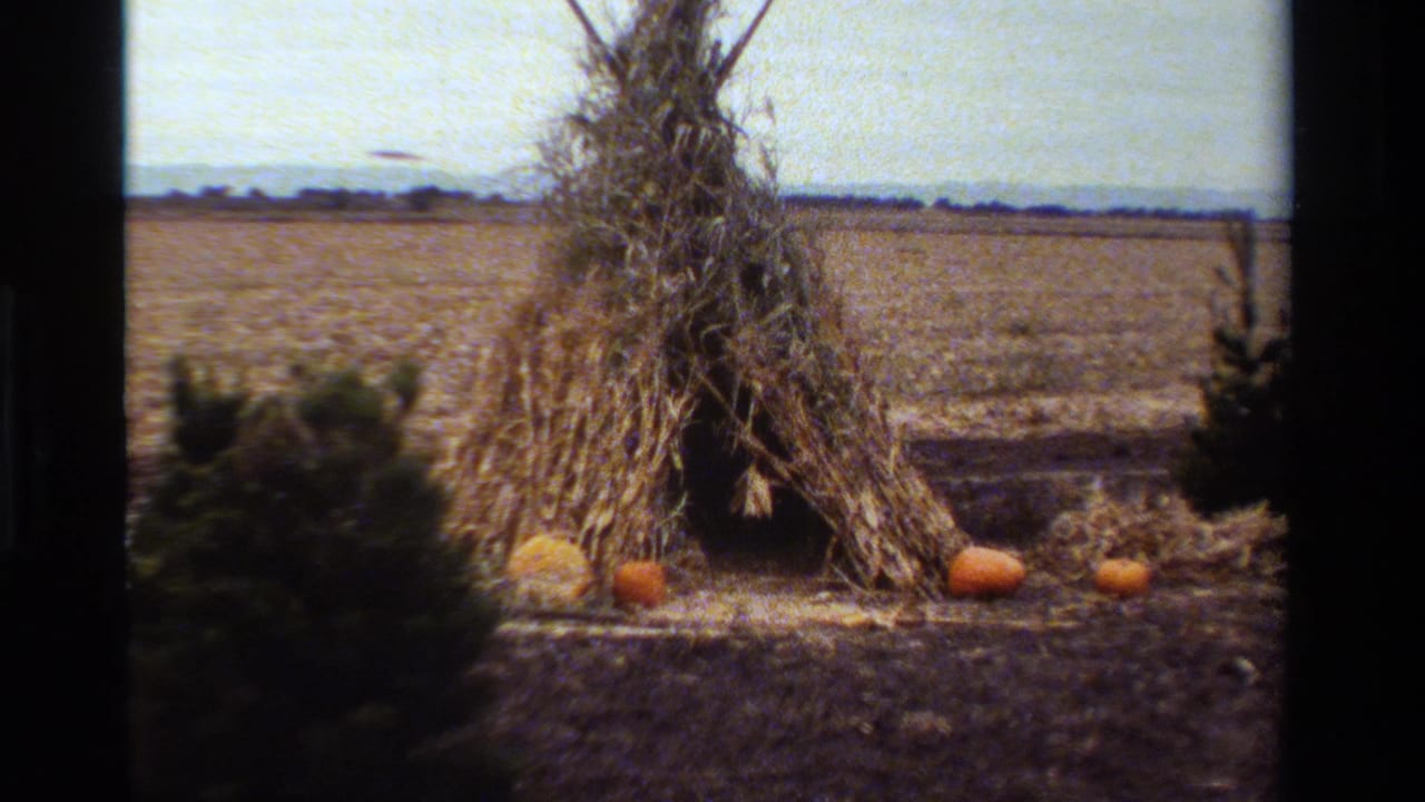 1984 California 8mm frame showing a harvested field with a corn-husk teepee structure and small pumpkins arranged nearby.