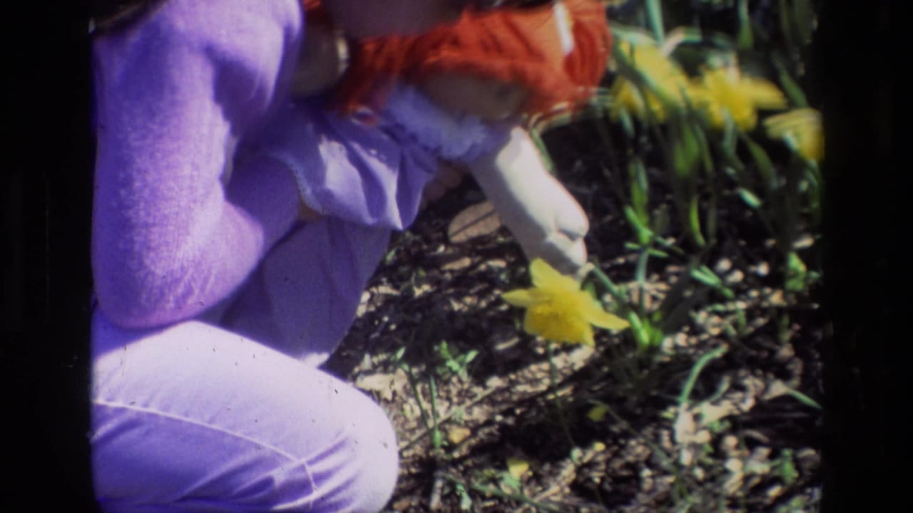 Woman in purple bends beside yellow daffodils while holding a red-haired doll.