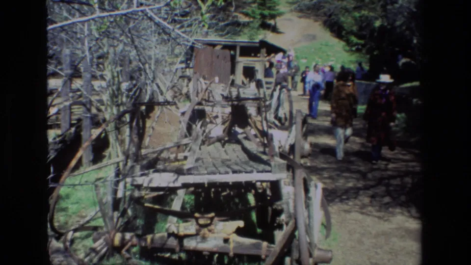 The 8mm frame shows visitors at Daffodil Hill walking past railings, rough wooden equipment, and a small shed in bright daylight.