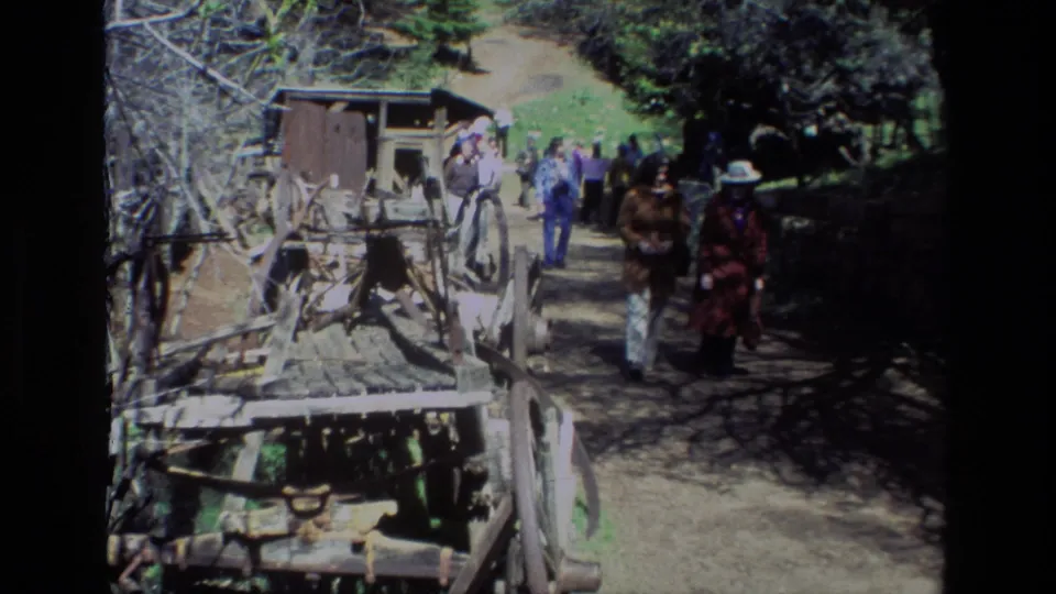 Visitors at Daffodil Hill in 1985 pass weathered wooden equipment and trees as the handheld 8mm shot looks down the path.