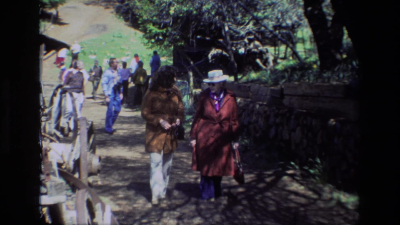 Two visitors approach the camera while other people walk behind them on a rural path.