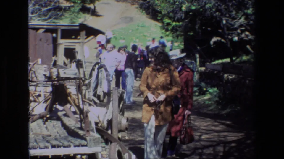 Visitors move past rustic rails and an old farm display on the Daffodil Hill walking path, with trees and bright hillside light behind them.