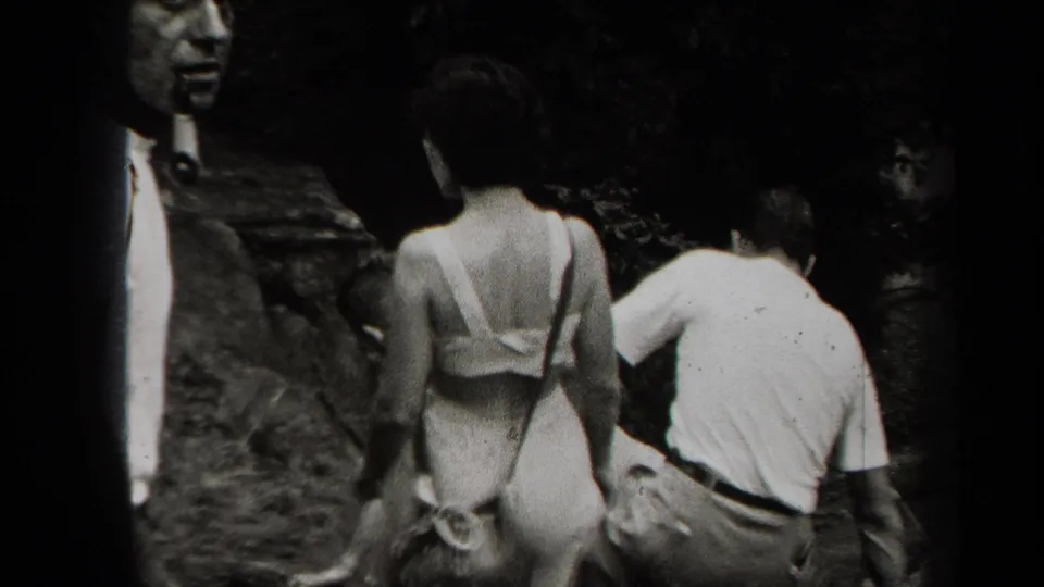 Adults in 1930s-style summer clothing move toward a dark rocky cave entrance, with one woman seen from behind carrying a strap bag.