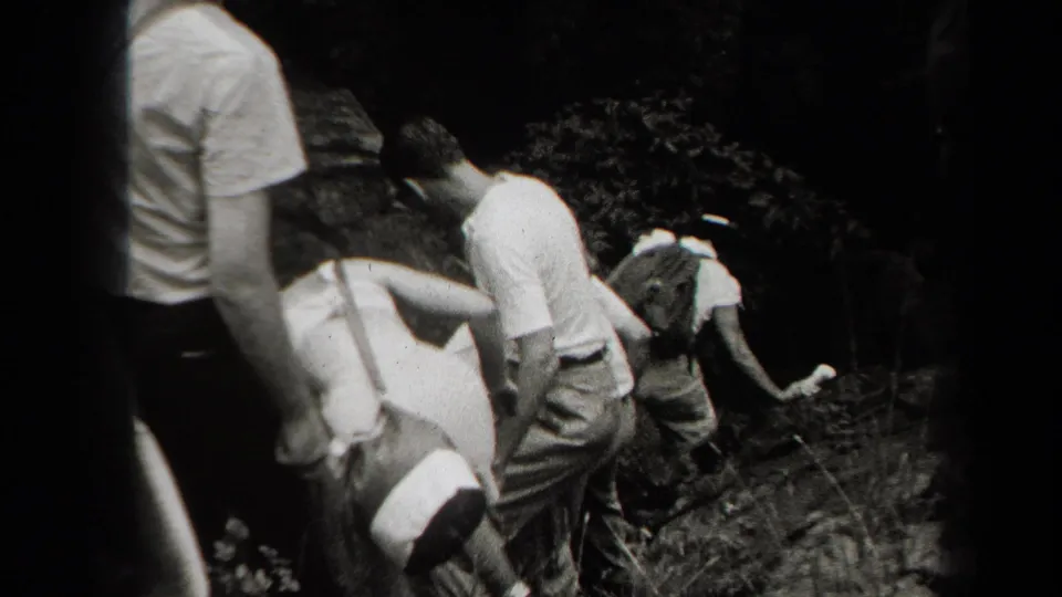 Several adults carefully descend a rocky, shadowed path in the New York cave setting, filmed from close behind in handheld 8mm footage.