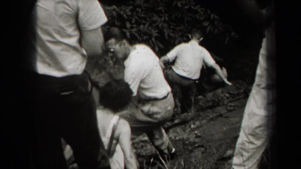 The group continues down the uneven cave approach, with figures in light shirts and trousers framed by dark rock and shadow.