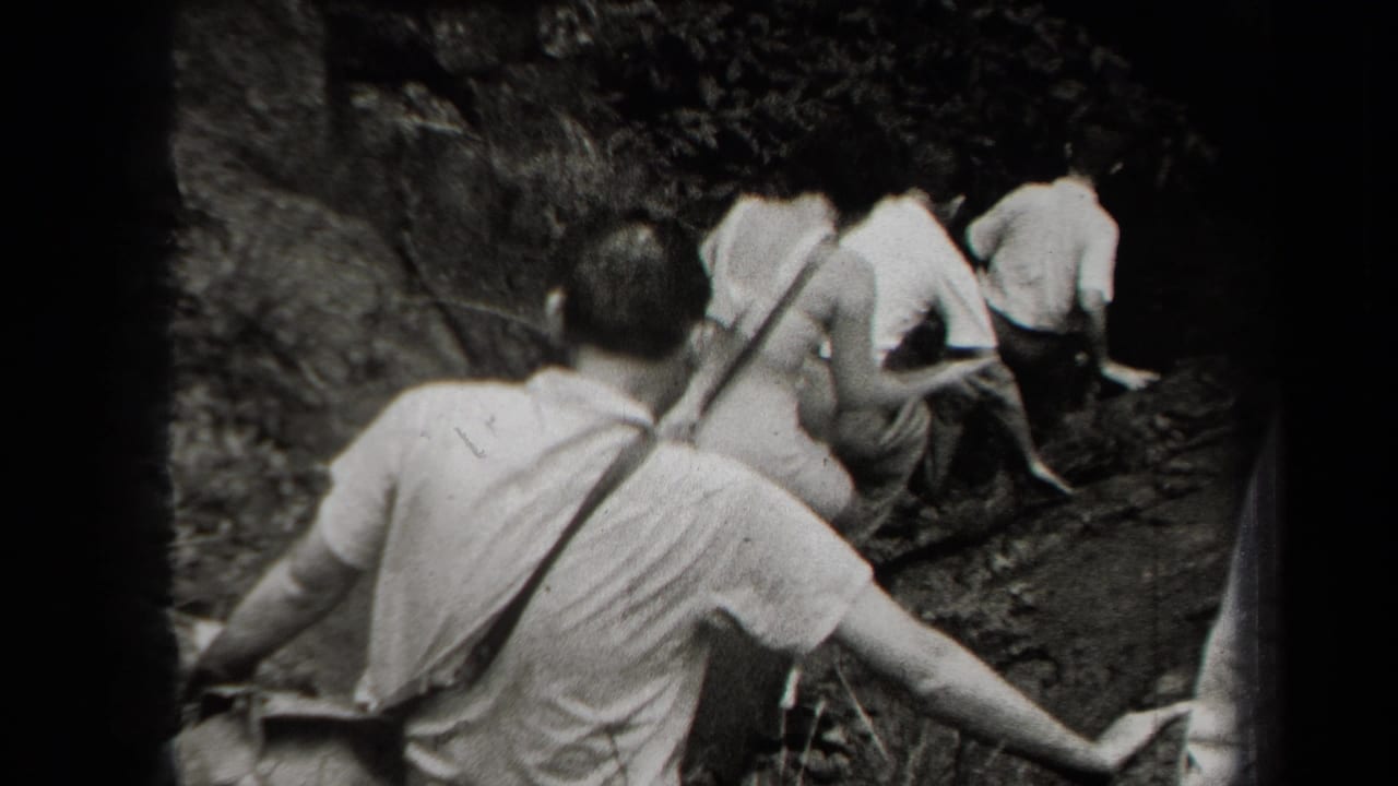 1938 New York home-movie frame showing men in light shirts moving up a steep rocky hillside through foliage.