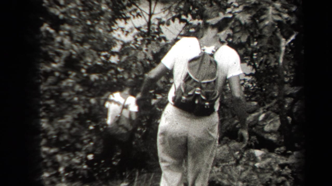 1938 New York 8mm frame showing men viewed from behind as they move carefully down a steep wooded slope.