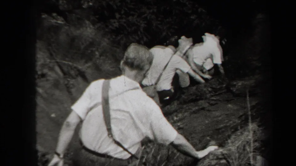 Rear-view 1938 New York home-movie frame of men in shirts and suspenders descending a wooded hillside.