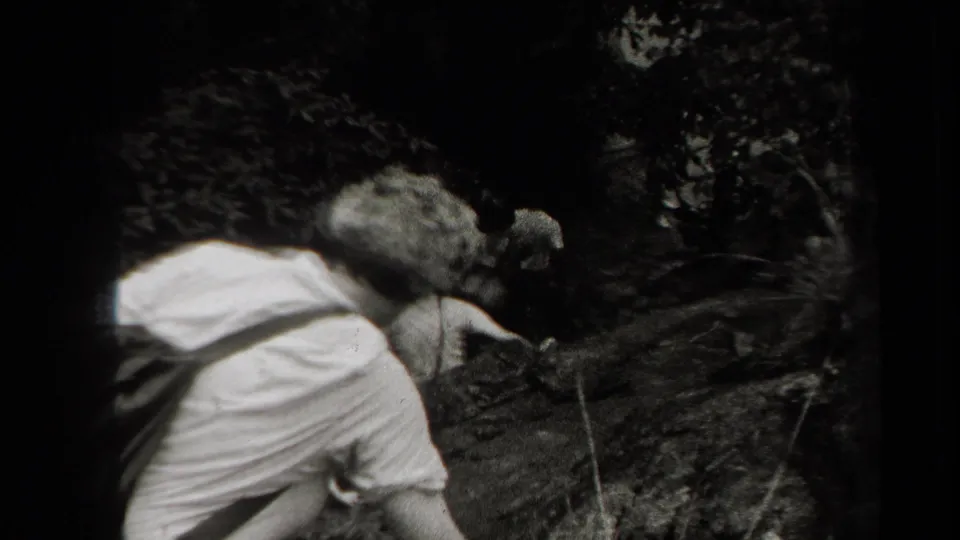 Home-movie frame from 1938 New York showing men crouching and balancing while descending a shadowed wooded hill.