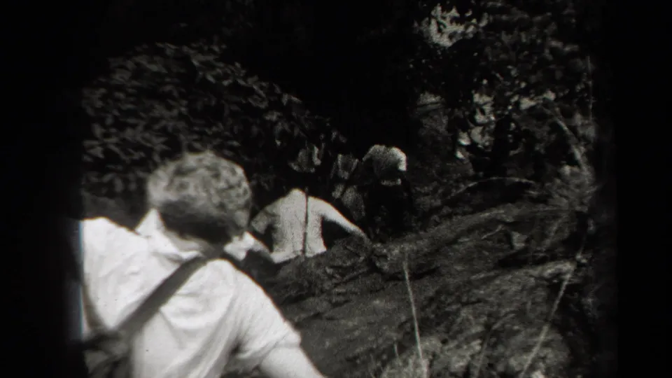 1938 New York home-movie frame showing friends from behind as they climb through a shaded rocky wooded area.