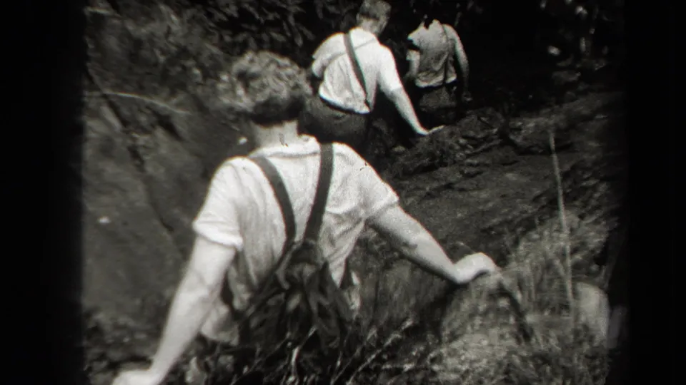 1938 home-movie frame showing a hiker close to the camera following companions along a rugged New York woodland path.