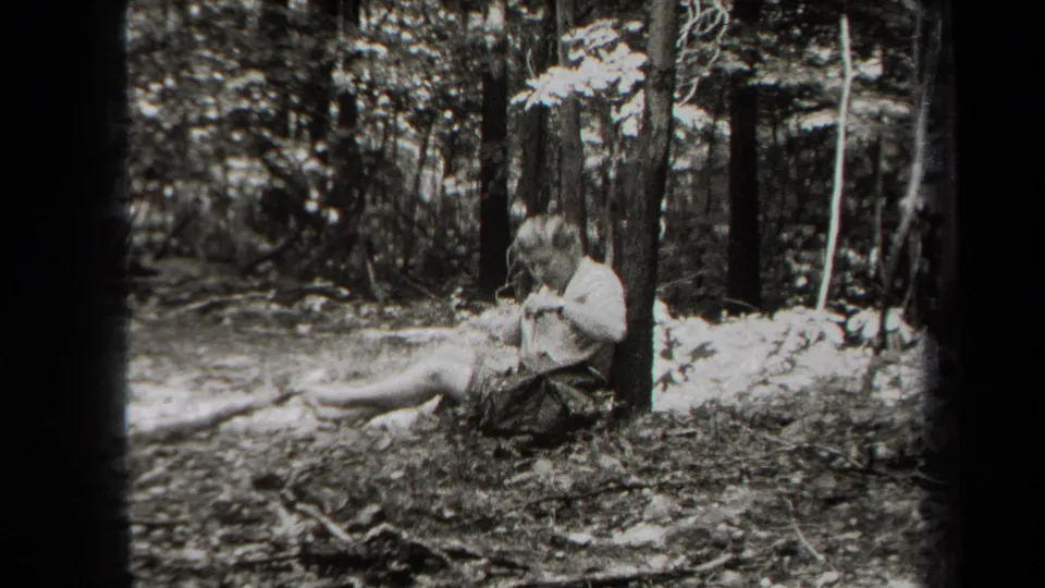 A person relaxes against a tree in the woods, holding reading material in this 1938 New York home-movie frame.