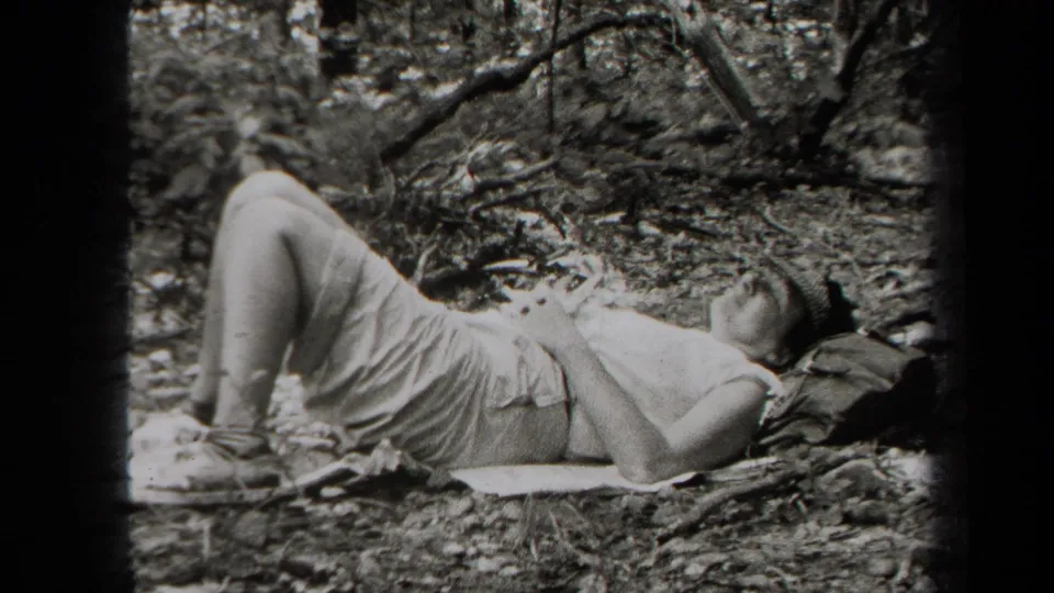 Black-and-white 8mm frame from 1938 New York showing a person lying back on a blanket in a wooded outdoor setting.