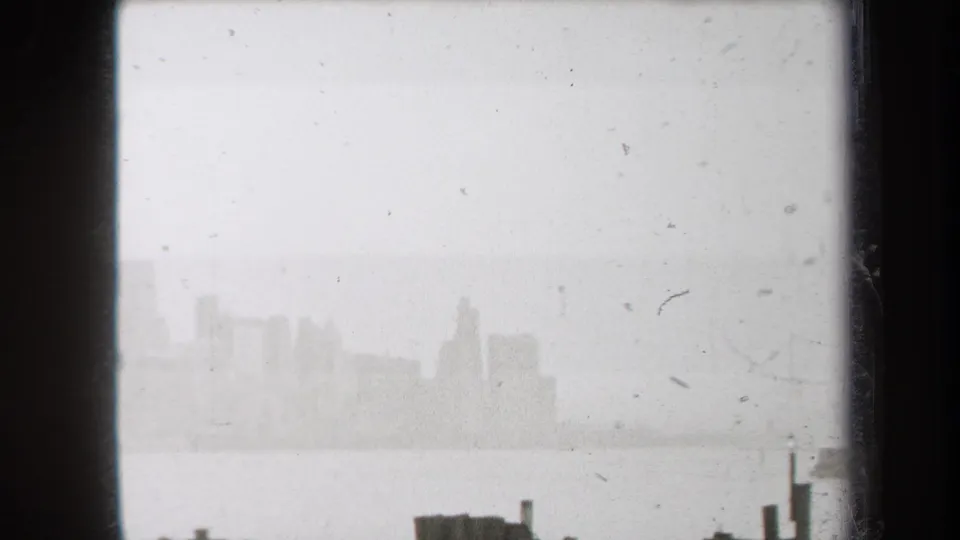 Hazy 1938 New York view of a distant skyline across water, seen through dark vertical edges and film grain.