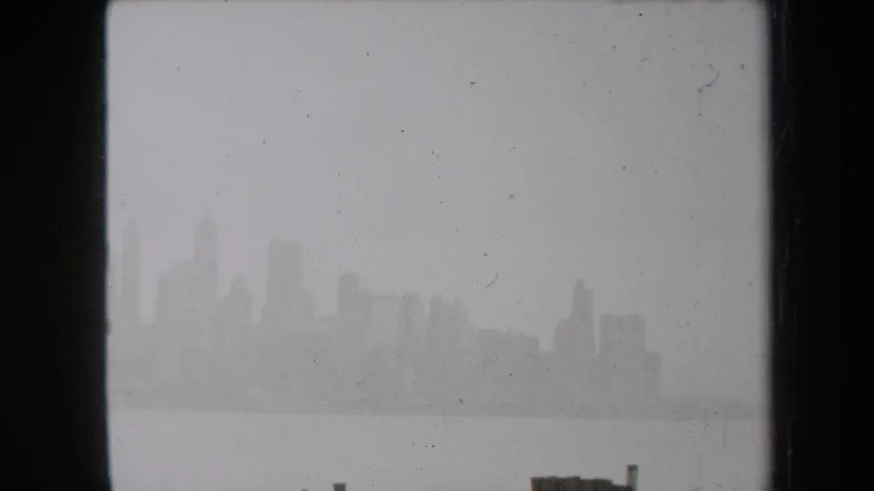 Fog-softened New York skyline across harbor water in 1938 8mm home-movie footage, with dark frame edges and dust specks.