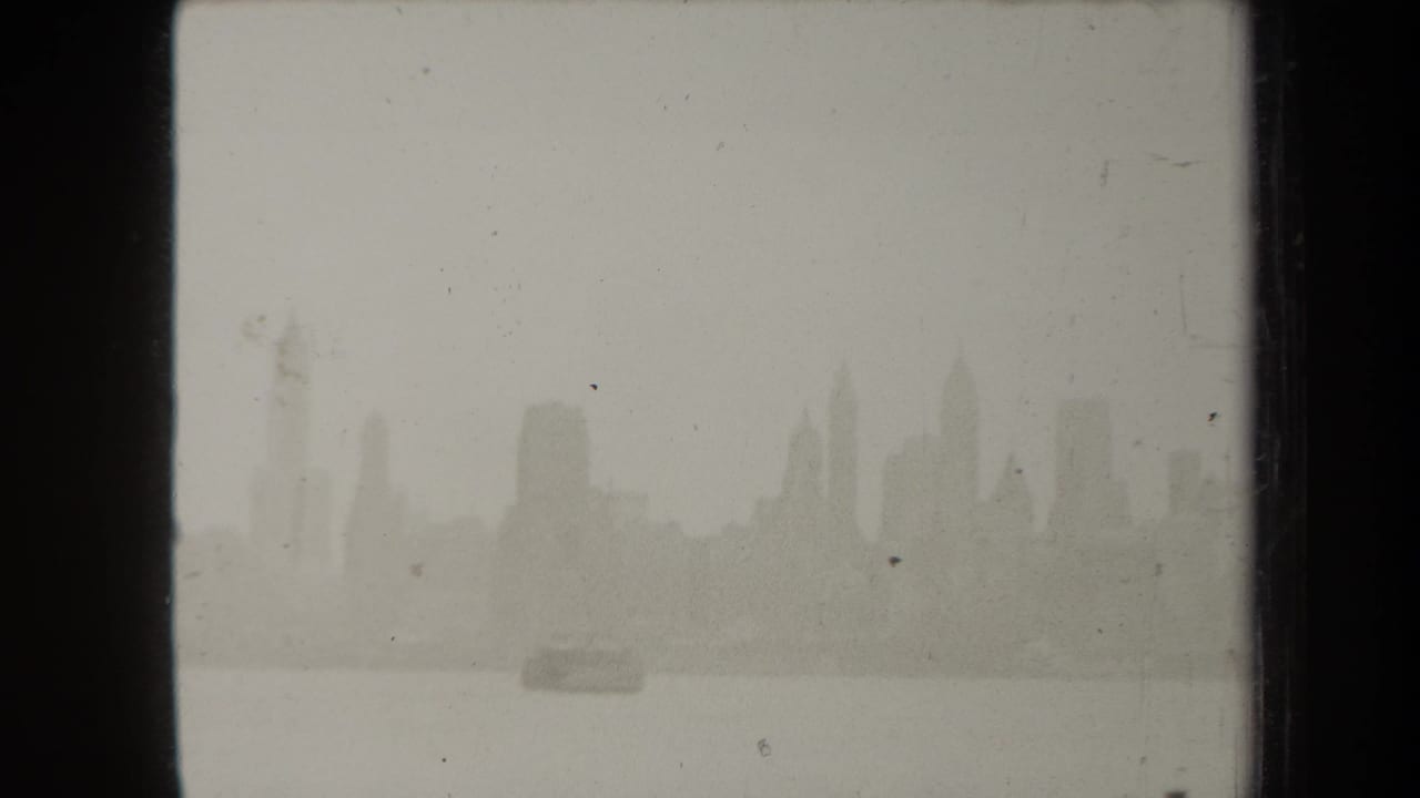 1938 New York skyline appears faintly across the water, framed by dark 8mm film borders and visible dust.