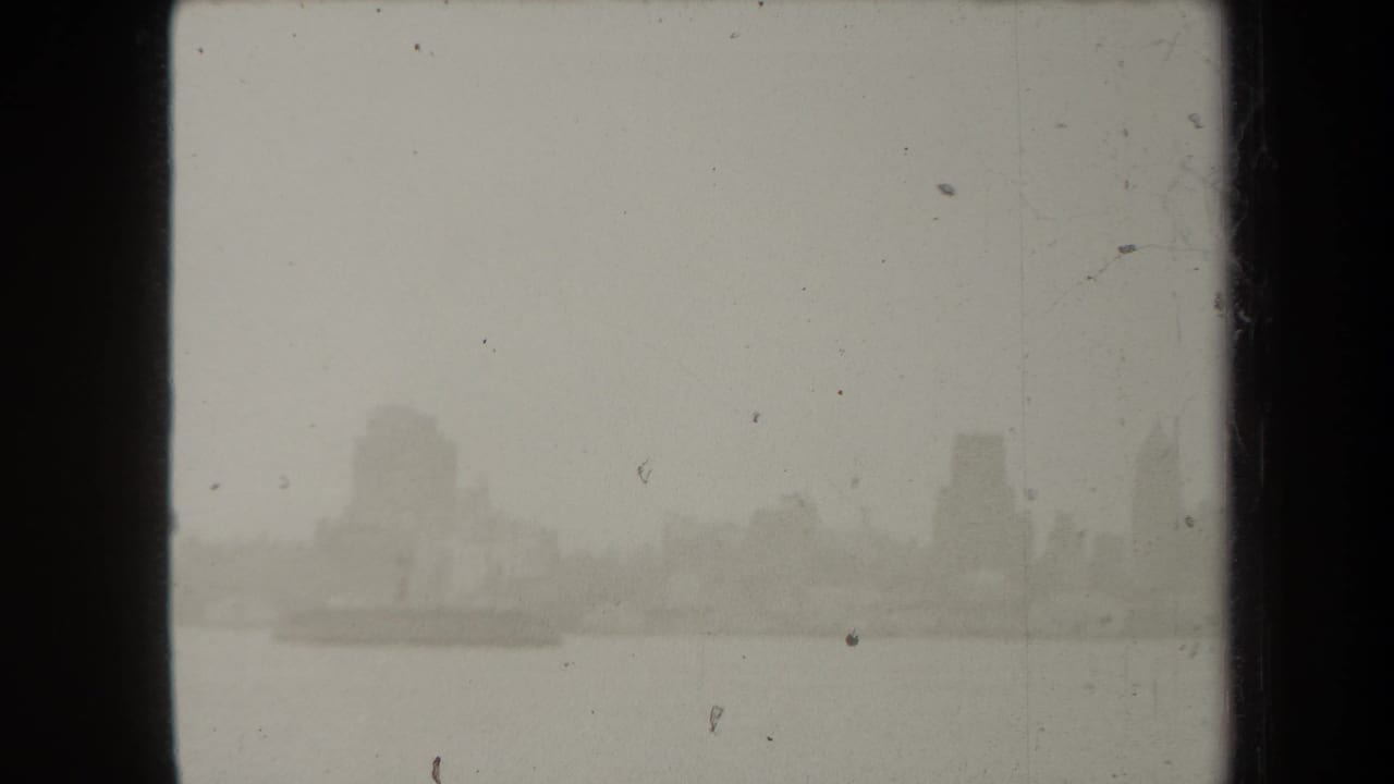 1938 New York home-movie frame showing a hazy waterfront skyline emerging through fog across open water.