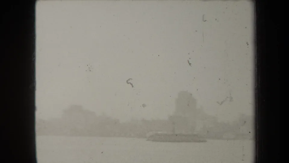 Fog-obscured New York skyline across water, with a darker low boat or ferry-like silhouette in the foreground distance.