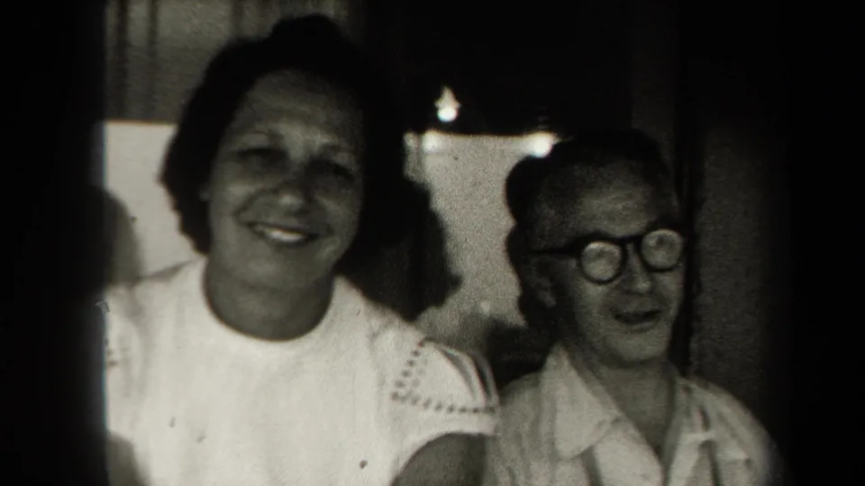 Smiling woman and older man with glasses sit inside an enclosed boat area in 1938 New York home-movie footage.