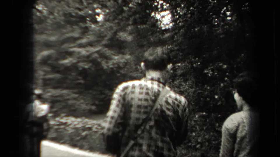 A rear view shows a man in a patterned shirt walking on a shaded park path, with another person at the edge of frame.