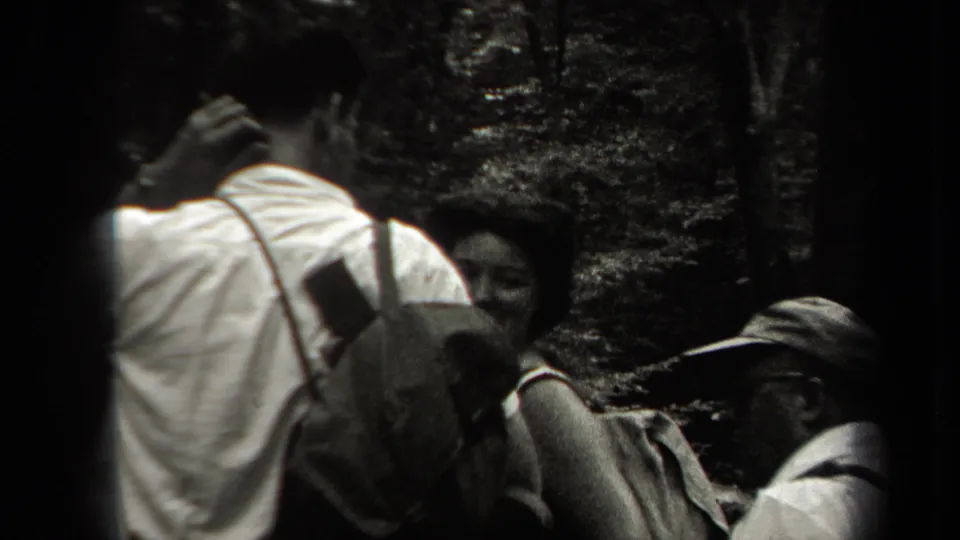 A close handheld view shows adults with backpacks and hats gathered on a wooded path in supported 1938 New York footage.