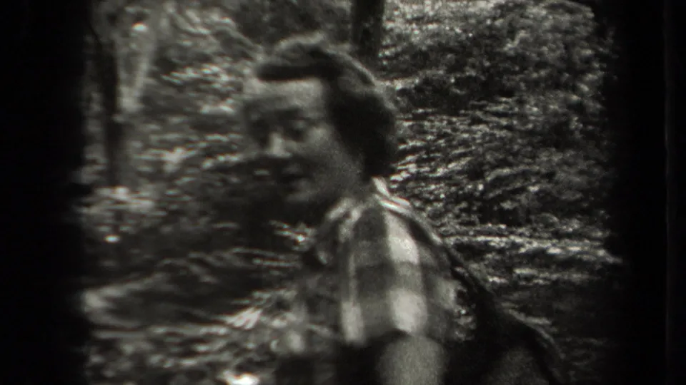 A face briefly turns toward the camera in a soft, grainy 1938 New York forest hiking scene.