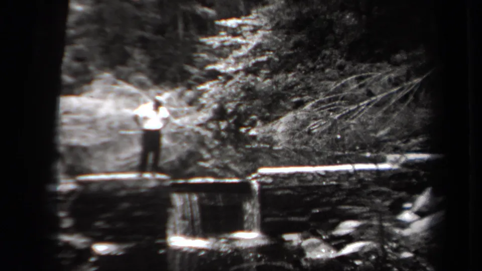1938 New York home-movie frame with a man standing on a stone bridge over a wooded stream or waterfall area.