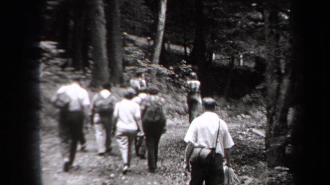 Adults in light shirts and period clothing walk away on a wooded trail in 1938 New York home-movie footage.
