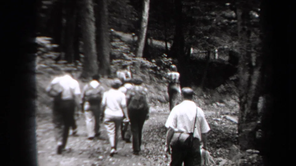 Adults in light shirts and period clothing walk away on a wooded trail in 1938 New York home-movie footage.